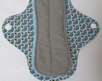May include: Reusable cloth menstrual pad with a gray absorbent core and a teal and gold patterned exterior. The pad has a light blue trim and a white snap closure. The pad is designed for feminine hygiene.