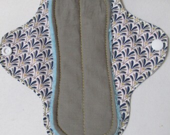 May include: Reusable cloth menstrual pad with a gray absorbent core, light blue trim, and a patterned top layer in navy, gold, and white. The pad has a snap closure and is designed for comfort and eco-friendliness.