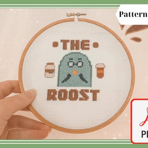 May include: Cross-stitch pattern in a wooden hoop featuring a teal bird character with glasses, holding coffee cups. The text "THE ROOST" is stitched below the bird. The words "Pattern Only" and a PDF icon are also visible.