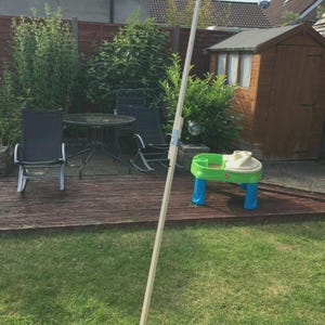 K&ouml;nnte beinhalten: Ein langer, unfertiger Holzpfahl steht in einem Garten. Der Pfahl ist hell und scheint ein Baumaterial zu sein. Ein kleiner, farbenfroher Kinderspieltisch ist ebenfalls zu sehen.