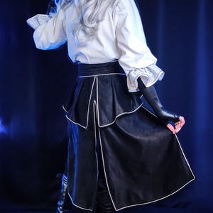 May include: A costume featuring a white blouse with ruffled sleeves and a black skirt with white trim. The outfit includes black gloves and boots. The model has long, silver hair. The background is a dark blue.