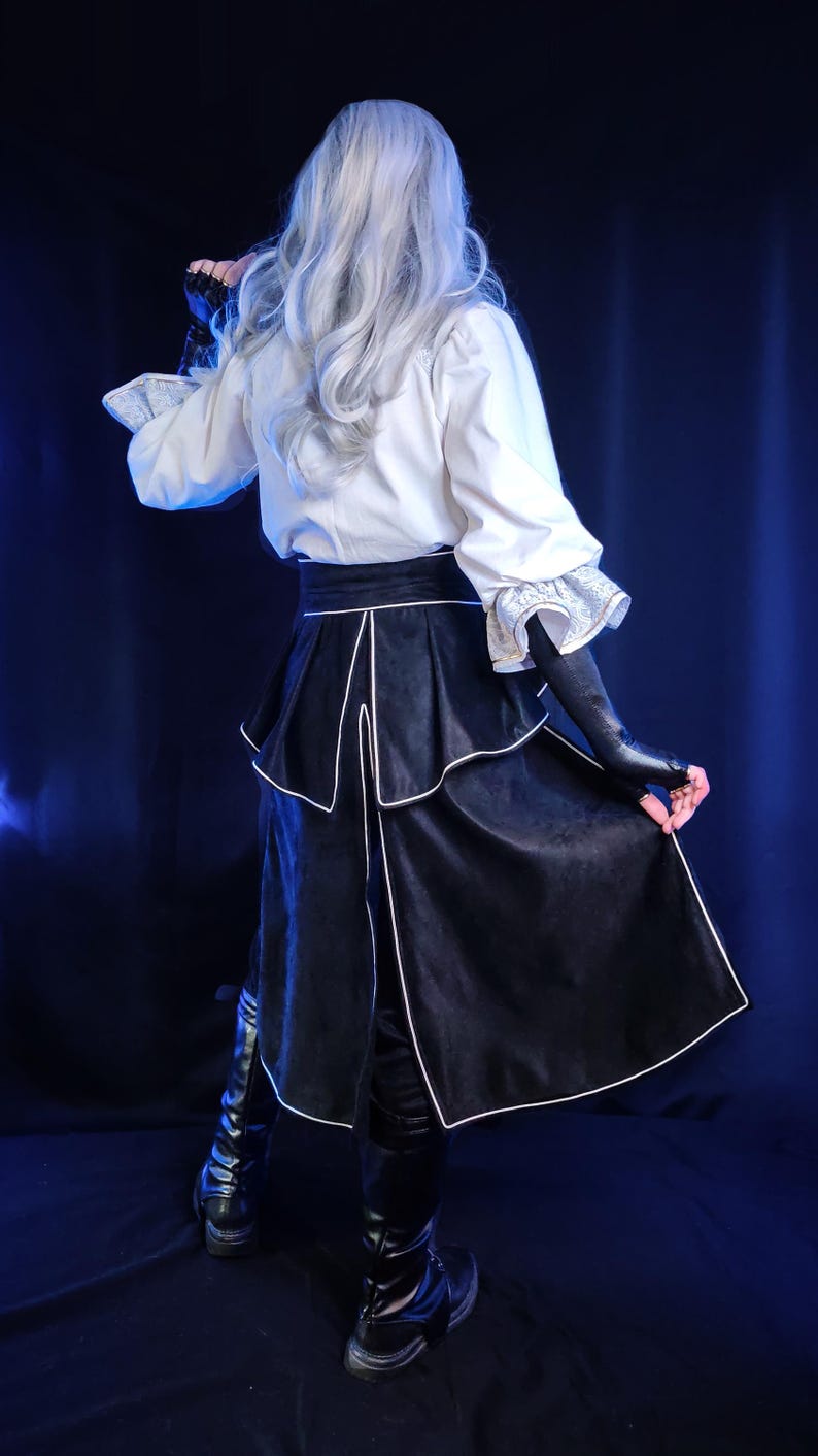 May include: A costume featuring a white blouse with ruffled sleeves and a black skirt with white trim. The outfit includes black gloves and boots. The model has long, silver hair. The background is a dark blue.