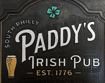 Puede incluir: Letrero de madera negro para Paddy's Irish Pub, con letras blancas y doradas. El letrero incluye el texto "South Philly", "Irish Pub" y "Est. 1776". Un trébol verde está en la parte superior e inferior. Se enumeran los propietarios y el conserje.