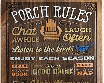 May include: Wooden sign with the words "PORCH RULES" in white and gold lettering. The sign includes phrases like "Chat Awhile," "Laugh Often," and "Listen to the birds." A blue bird is depicted on the sign. The sign is framed in a dark brown wood.