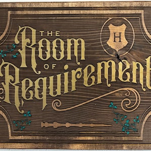 以下が含まれることがあります： 「The Room of Requirement」の文字が金色で書かれた、濃い色の木製サイン。装飾的な縁取り、魔法の杖、そして「H」の文字が入った紋章が特徴です。