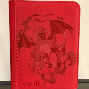 May include: Red Vault X trading card binder featuring a Charizard design with Charmander and Charmeleon. The binder has a zipper closure and the Vault X logo is visible on the front.