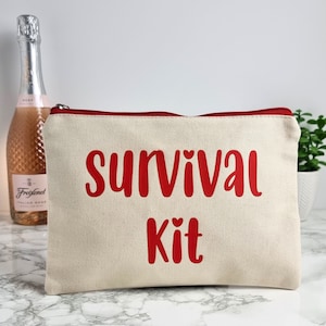 May include: A white canvas zippered pouch with a red zipper and red text that reads "survival kit" with two small hearts above the word "kit".