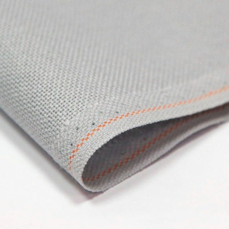 Peut inclure: Gros plan sur un tissu gris avec une texture subtile. Le tissu a une fine couture orange le long du bord.