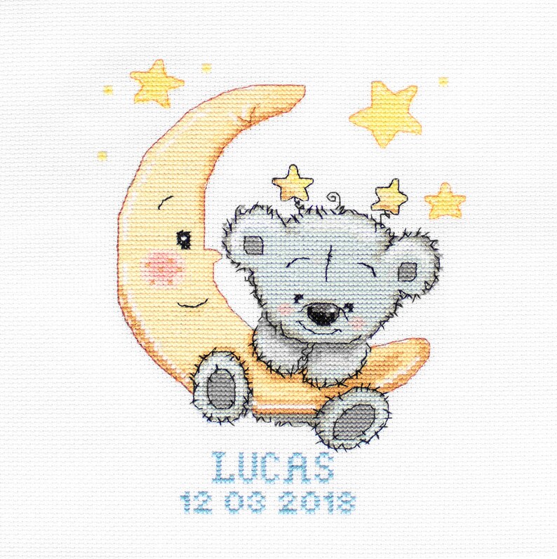 May include: Cross-stitch design of a smiling grey teddy bear on a yellow crescent moon, with yellow stars. The name "LUCAS" and the date "12 03 2018" are stitched in blue below the moon.
