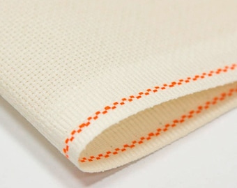 May include: Close-up of a white fabric with an orange stitched border. The fabric has a textured, woven appearance.