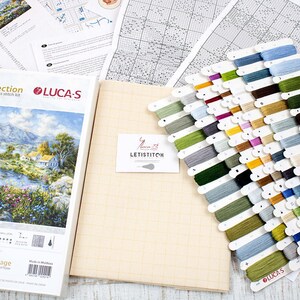 May include: A cross-stitch kit from the Gold Collection by Luca-S, depicting a landscape with a river and cottage. The kit includes aida cloth, thread, and a chart. It features a range of thread colours and is packaged with the "Enchanted Cottage" design.