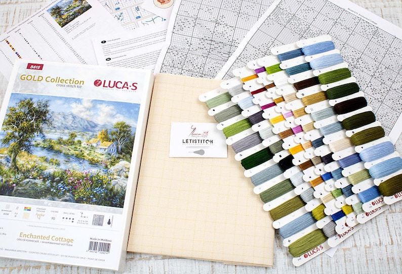 May include: A cross-stitch kit from the Gold Collection by Luca-S, depicting a landscape with a river and cottage. The kit includes aida cloth, thread, and a chart. It features a range of thread colours and is packaged with the "Enchanted Cottage" design.