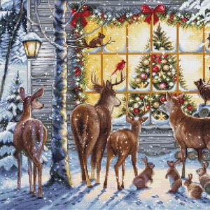 Pode incluir: Um padrão de ponto cruz de uma cena de inverno com veados, coelhos e outros animais selvagens em uma paisagem nevada. Uma árvore de Natal decorada é visível através de uma janela, com um cardeal vermelho empoleirado em um galho.