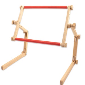 Puede incluir: Un soporte de bordado de madera con dos brazos acolchados rojos. El soporte es ajustable y se pliega para su almacenamiento.