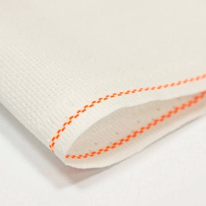 Peut inclure: Gros plan sur un tissu blanc avec un bord cousu orange. Le tissu a une texture fine et tiss&eacute;e.