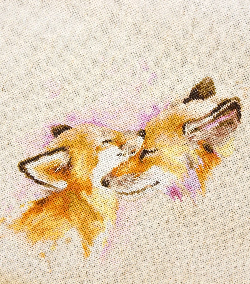 May include: Cross-stitch embroidery of two foxes cuddling, with a watercolour-like effect in shades of pink, orange, and brown.