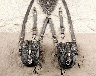 May include: A black leather harness featuring two attached pouches with intricate stitching, metal studs, and decorative accents. The harness includes adjustable straps, metal lobster clasps, and a central triangular back piece with a small embedded stone.
