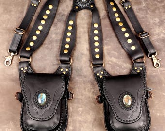 Puede incluir: Un arnés de doble funda de cuero negro con dos bolsas adornadas con piedras de labradorita ovaladas, tachuelas de latón y correas ajustables con clips giratorios. La pieza central trasera también contiene una labradorita a juego.