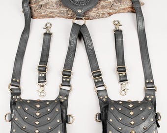 Puede incluir: Un arnés de cuero negro con dos bolsas simétricas de solapas escalonadas adornadas con tachuelas de color latón. La pieza central trasera incluye una piedra en forma de lágrima. El conjunto incluye correas ajustables, herrajes de latón y dos correas laterales desmontables.