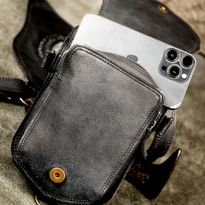 Smartphone fitting into secure quick-access rear pocket of black handcrafted leather holster bag with antique brass snap.