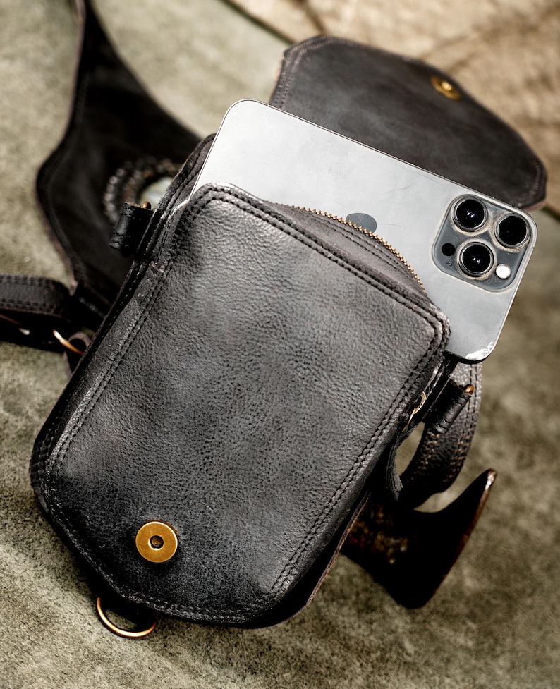 Smartphone fitting into secure quick-access rear pocket of black handcrafted leather holster bag with antique brass snap.