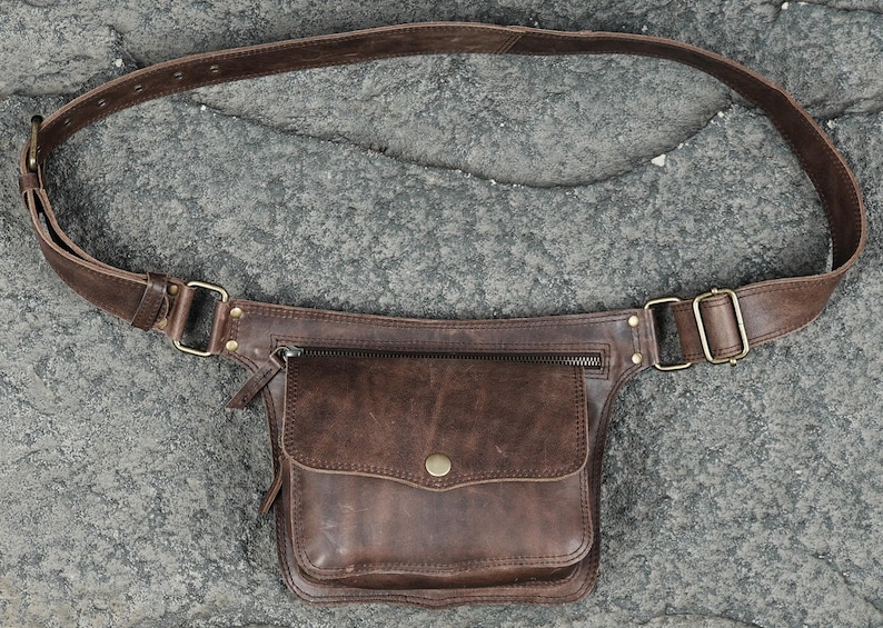 Brown leather utility waist pouch with flap pocket, antique brass hardware, and adjustable strap for hands-free festival wear.