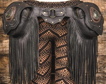 May include: Black leather hip belt with fringe, pockets, and decorative stone accents. The belt features a buckle closure and is adorned with metal studs. The design includes two zippered pockets and a fringed skirt.