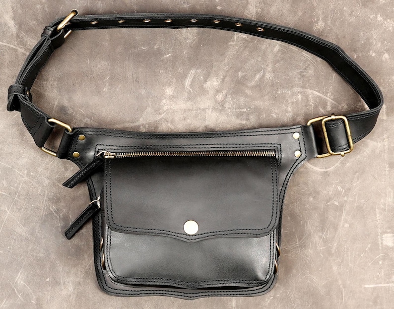 Black handmade leather hip bag featuring antique brass buckle, front zipper pocket, snap flap pouch, and grommet waist strap on grey background. 

Leather Hip Bag, Utility Waist Belt, Festival Fanny Pack, Black Leather Pouch, Pocket Belt, Biker Hip Belt, Travel Waist Bag, Steampunk Belt, Boho Festival Bag, Men Hip Bag, Leather Utility Bag, Handmade Belt Bag, Crossbody Hip Bag
