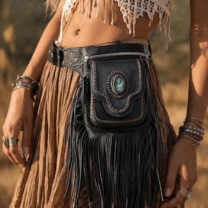 May include: A black leather belt bag with a fringed bottom and a small zipped pocket. The bag features a decorative turquoise stone and is worn with a brown skirt and a white crochet top.