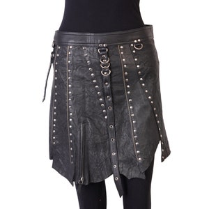May include: Black leather skirt with silver-tone studs, zippers, and metal rings. The skirt has an asymmetrical hemline and a belt-like closure. The garment is designed with a textured, slightly wrinkled appearance.
