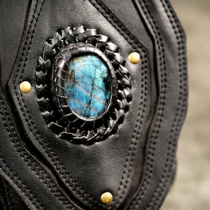 Close-up of natural blue-flash labradorite gemstone centerpiece set in hand-stitched black leather pouch with antique brass studs.