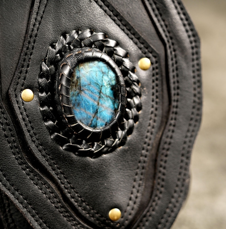 Close-up of natural blue-flash labradorite gemstone centerpiece set in hand-stitched black leather pouch with antique brass studs.