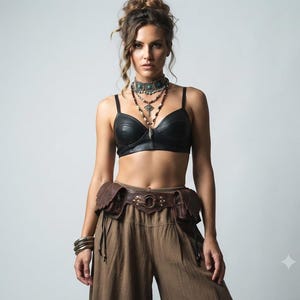 Puede incluir: Un top tipo bustier negro con aspecto de cuero combinado con un cinturón utilitario marrón con dos bolsillos laterales y un anillo central. El conjunto incluye un collar de cuentas en capas con un colgante y pulseras metálicas en la muñeca.