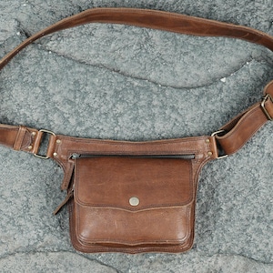 Handmade brown leather utility pocket belt with front flap pocket, metal snap closure, and antique brass hardware for bohemian style.