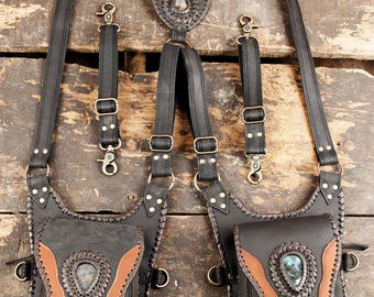 Puede incluir: Un arnés de cuero negro con dos bolsas simétricas con detalles en cuero marrón claro y piedras en forma de lágrima. El arnés incluye correas ajustables con herrajes de metal color latón, bordes de cuero trenzado y dos correas verticales extraíbles.