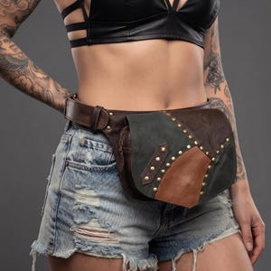 May include: A brown leather waist bag featuring a dark green and tan leather flap overlay. The bag is secured with a wide leather belt and decorated with multiple small brass-coloured metal studs along the edges of the front flap and strap.