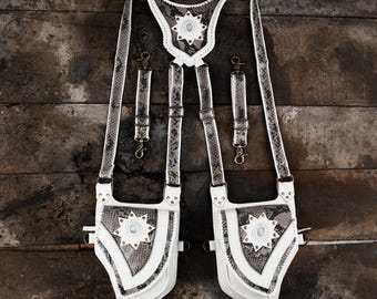 May include: A white and snakeskin-patterned leather harness with decorative starburst accents. The harness features adjustable straps, metal hardware, and two matching pouches. The design is set against a rustic wooden background.