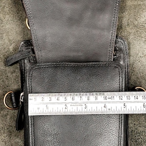 Metal ruler measuring compartment opening width of open black leather utility holster pouch.