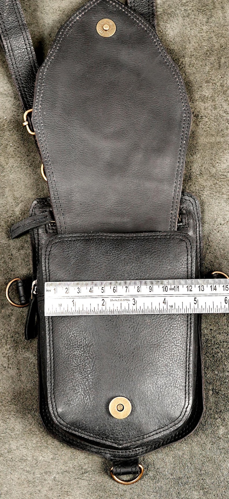 Metal ruler measuring compartment opening width of open black leather utility holster pouch.