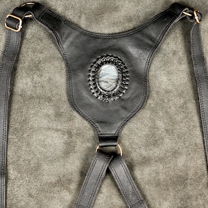 Center back connector plate of black leather holster harness featuring inlaid natural labradorite stone and antique brass D-ring.
