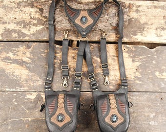 May include: A black and brown leather harness featuring two pouches with brass-toned hardware, decorative stitching, and a central blue stone accent on each pouch and the chest piece. The harness includes adjustable straps with metal clips.