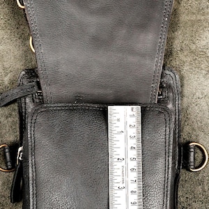 Metal ruler measuring interior vertical height of open black leather holster pocket with antique brass snap closure.