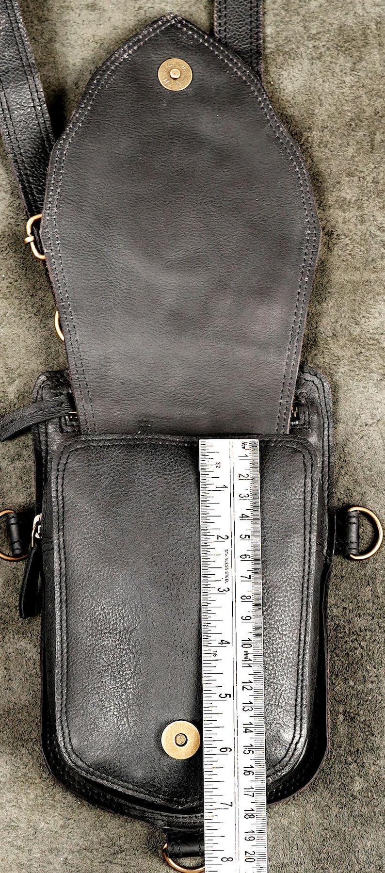 Metal ruler measuring interior vertical height of open black leather holster pocket with antique brass snap closure.