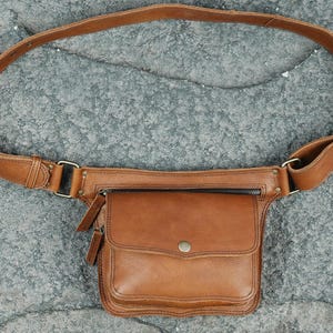 Handmade light brown leather waist belt bag with front flap snap pocket, brass zipper, and adjustable buckle strap for festival travel utility.