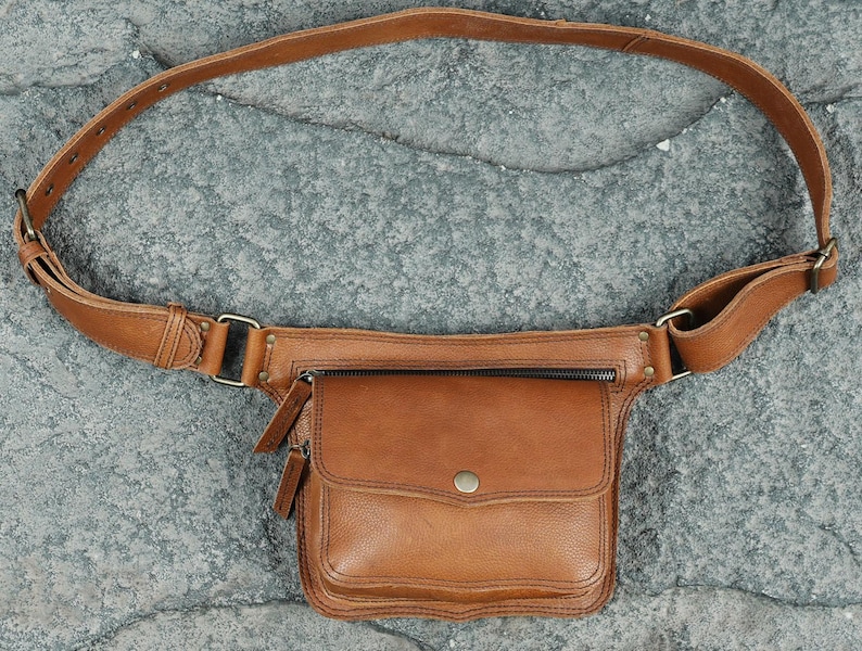 Handmade light brown leather waist belt bag with front flap snap pocket, brass zipper, and adjustable buckle strap for festival travel utility.
