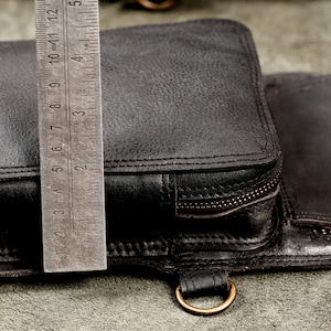 Metal ruler measuring side depth and zippered pocket thickness of black leather shoulder holster bag.