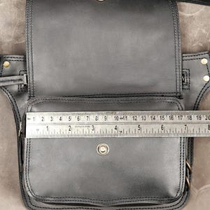 Measurement scale on open black utility belt bag showing pocket width across front zippered compartment and magnetic snap flap.