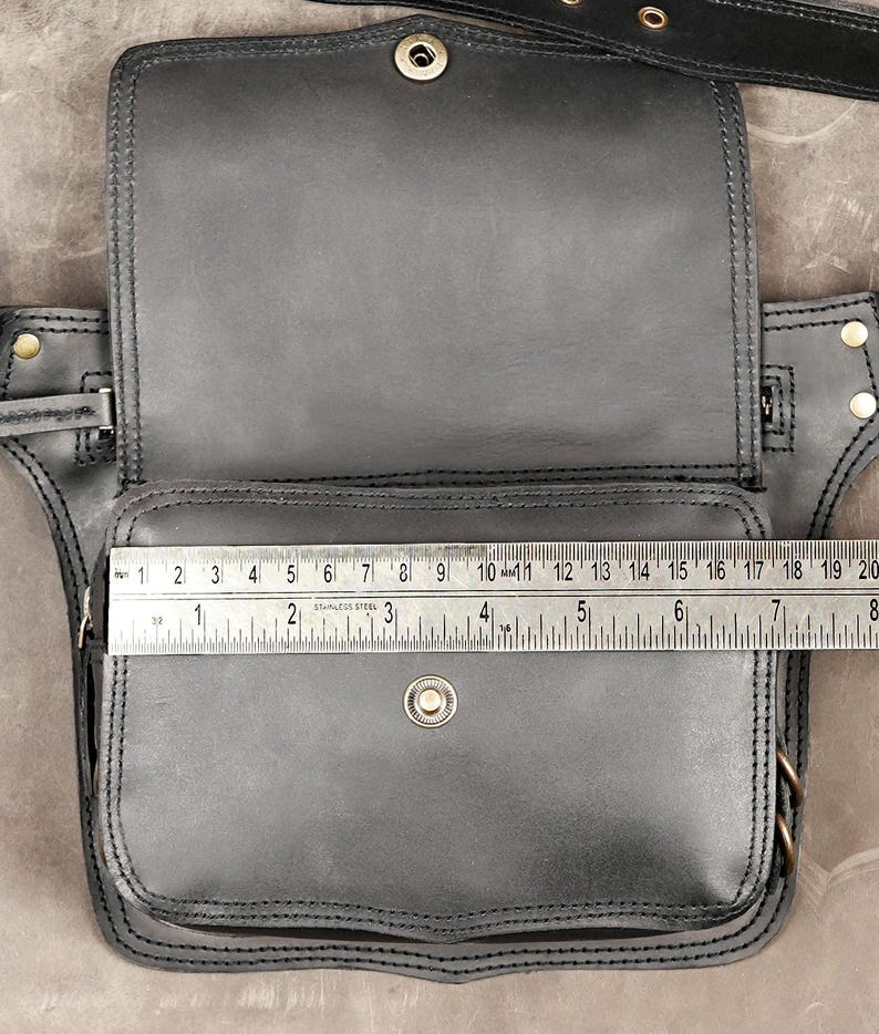 Measurement scale on open black utility belt bag showing pocket width across front zippered compartment and magnetic snap flap.