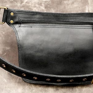 Back view of a handmade black leather hip bag with a hidden security zipper pocket, antique brass hardware, and an adjustable eyelet belt strap.

leather hip bag, black waist pouch, festival belt bag, utility hip pouch, steampunk waist bag, boho fanny pack, handmade leather bag, travel waist pack, gothic hip bag, leather fanny pack, rave utility belt, brass hardware bag, biker waist bag