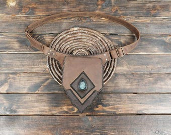 May include: A brown leather belt with an attached pouch featuring a diamond-shaped flap and a central teardrop-shaped blue stone accent. The pouch is secured with dark stitching and the belt includes a metal buckle and adjustable strap holes.